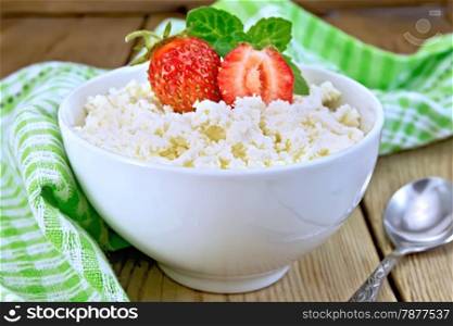 Cottage cheese in a white bowl with strawberries and mint, spoon, green cloth on a wooden boards background