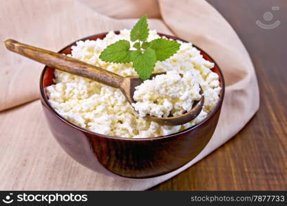 Cottage cheese in a wooden bowl with a spoon and mint on a cloth on a wooden boards background