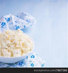 Cottage cheese in white bowl over blue background, selective focus, copy space