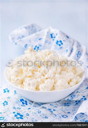 Cottage cheese in white bowl over light blue background, selective focus