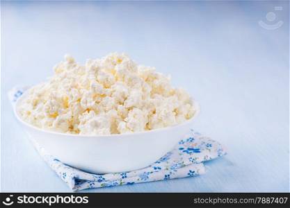 Cottage cheese in white bowl over light blue background, selective focus
