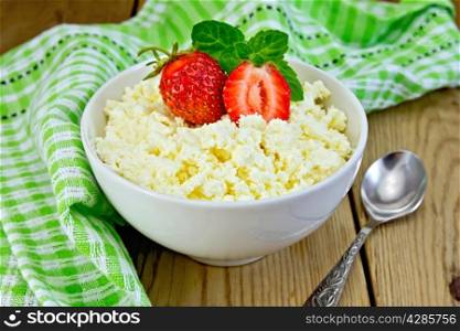 Cottage cheese in white bowl with strawberries and mint, spoon, napkin on the background of wooden boards