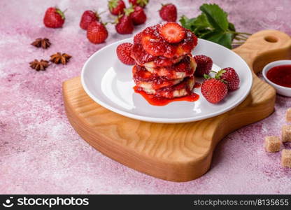 Cottage cheese pancake with strawberry jam on a concrete background. Cottage cheese pancakes with sliced strawberries and strawberry jam on a plate on a concrete background