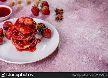 Cottage cheese pancake with strawberry jam on a concrete background. Cottage cheese pancakes with sliced strawberries and strawberry jam on a plate on a concrete background