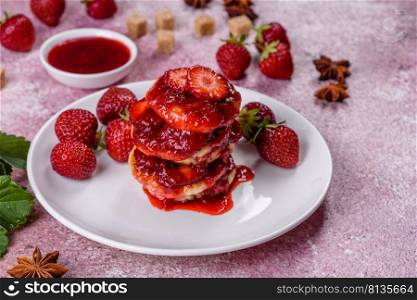 Cottage cheese pancake with strawberry jam on a concrete background. Cottage cheese pancakes with sliced strawberries and strawberry jam on a plate on a concrete background