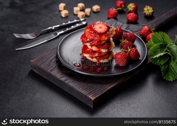 Cottage cheese pancake with strawberry jam on a concrete background. Cottage cheese pancakes with sliced strawberries and strawberry jam on a plate on a concrete background