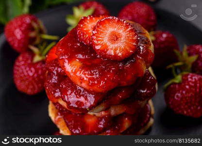 Cottage cheese pancake with strawberry jam on a concrete background. Cottage cheese pancakes with sliced strawberries and strawberry jam on a plate on a concrete background