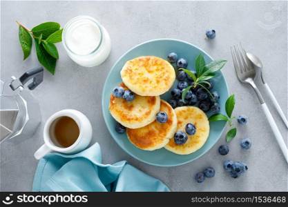 Cottage cheese pancakes, sweet curd fritters with berries, syrniki with honey and fresh blueberry on breakfast table