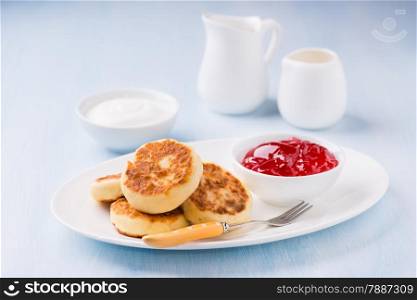 Cottage cheese pancakes with currant jam and sour cream, light blue background, selective focus