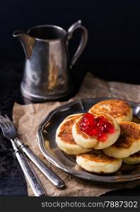 Cottage cheese pancakes with currant jam on vintage metal plate, selective focus