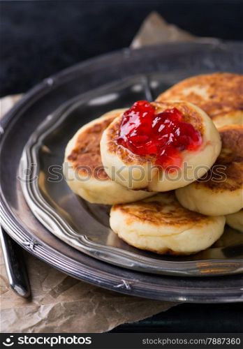 Cottage cheese pancakes with currant jam on vintage metal plate, selective focus