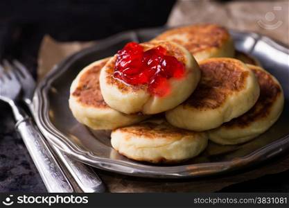 Cottage cheese pancakes with currant jam on vintage metal plate, top view, selective focus