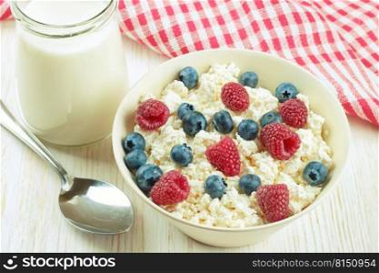 cottage cheese with berries in a bowl and jar of milk on white wooden background. Dairy products, healthy food.. cottage cheese with berries