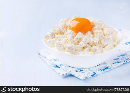 Cottage cheese with egg yolk in white bowl over light blue background, selective focus