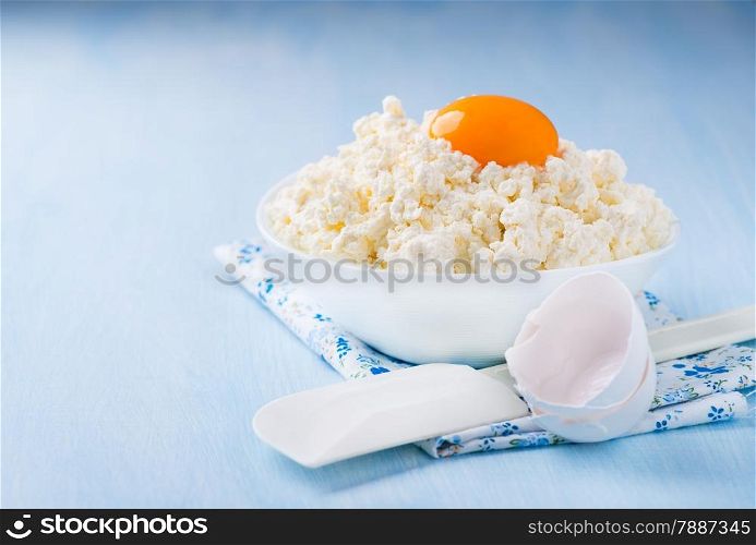 Cottage cheese with egg yolk in white bowl over light blue background, selective focus