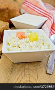 Cottage cheese with multi-colored cubes of sugar, sour cream in a white square bowls, napkin, spoon, bread on the background of wooden boards