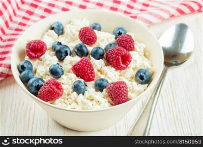 cottage cheese with raspberries and blueberries in a bowl on white wooden background. Dairy products, healthy food.. cottage cheese with berries
