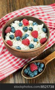 cottage cheese with raspberries and blueberries in brown clay bowl and wooden spoon on red checkered towel. Dairy products, healthy food.. cottage cheese with berries