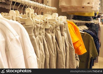 Cotton clothes on hangers in the store of the shopping center. Gray pants, white sweaters, multi-colored T-shirts.