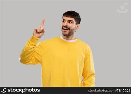 count and people concept - smiling young man in yellow sweatshirt showing one finger over grey background. young man showing one finger in yellow sweatshirt