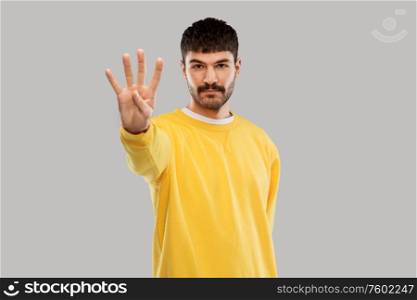 count and people concept - young man in yellow sweatshirt showing four fingers over grey background. man in yellow sweatshirt showing four fingers