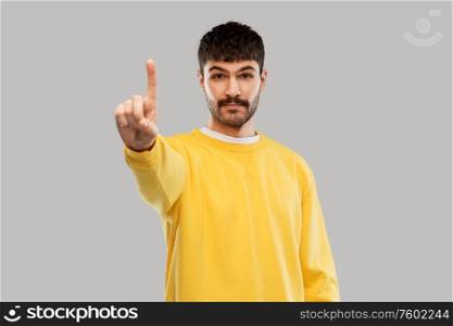 count and people concept - young man in yellow sweatshirt showing one finger over grey background. young man in yellow sweatshirt showing one finger