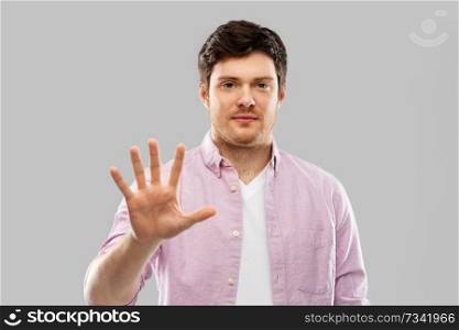 count and people concept - young man showing five fingers over grey background. young man showing five fingers over grey
