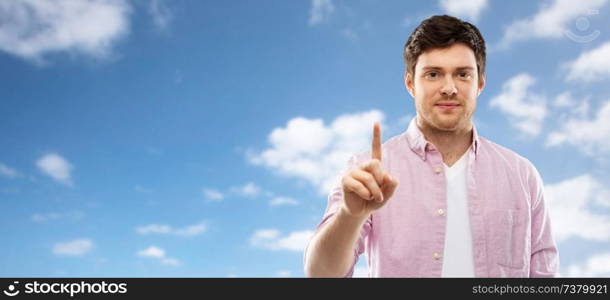 count and people concept - young man showing one finger over blue sky and clouds background. young man showing one finger over sky