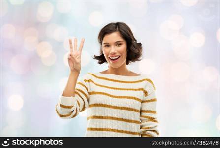 counting and people concept - happy smiling young woman in striped pullover showing three fingers over festive lights background. happy smiling woman showing three fingers