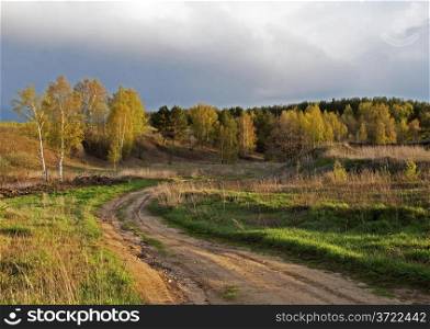Country dirt road in the forest at sunset, dark sky