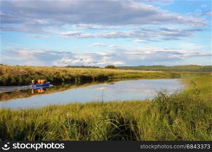 Country landscape. Soroti river and motor boat with tourists near the Mikhailovskoye village, Pskov region, Russia. Summer evening.