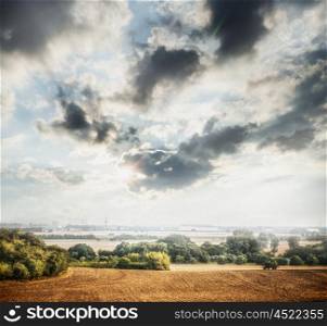 Country Landscape with plowed field, trees and beautiful sky with clouds and sunlight