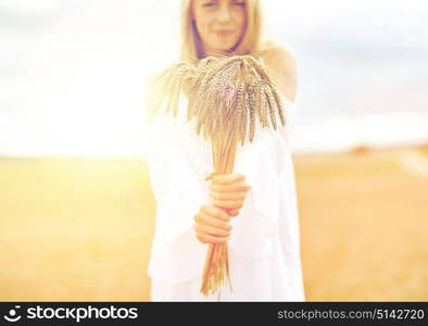 country, nature, summer holidays, vacation and people concept - close up of smiling young woman in white dress with spikelets on cereal field. close up of happy woman with cereal spikelets