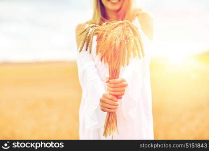 country, nature, summer holidays, vacation and people concept - close up of smiling young woman in white dress with spikelets on cereal field. close up of happy woman with cereal spikelets