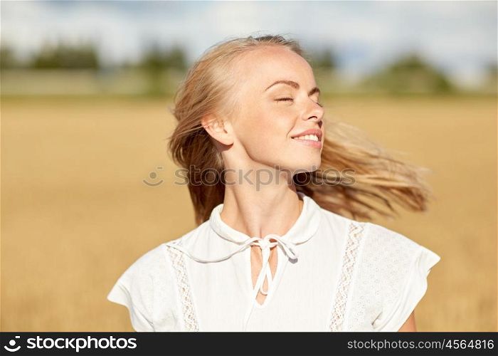 country, nature, summer holidays, vacation and people concept - happy smiling young woman or teenage girl in white enjoying sun on cereal field