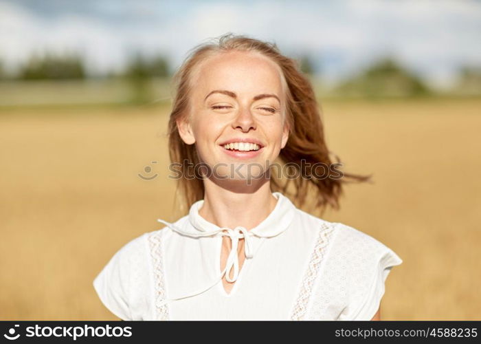 country, nature, summer holidays, vacation and people concept - happy smiling young woman or teenage girl in white enjoying sun on cereal field