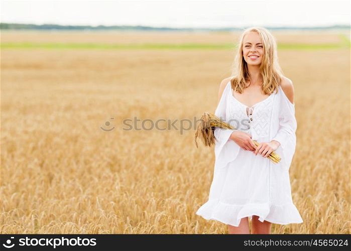 country, nature, summer holidays, vacation and people concept - smiling young woman in white dress with spikelets walking along on cereal field