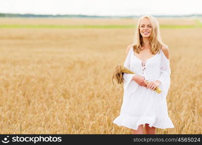 country, nature, summer holidays, vacation and people concept - smiling young woman in white dress with spikelets walking along on cereal field