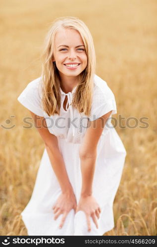 country, nature, summer holidays, vacation and people concept - smiling young woman in white dress on cereal field