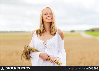 country, nature, summer holidays, vacation and people concept - smiling young woman in white dress with spikelets walking along on cereal field