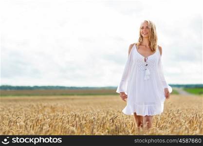 country, nature, summer holidays, vacation and people concept - smiling young woman in white dress on cereal field