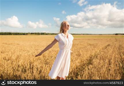 country, nature, summer holidays, vacation and people concept - smiling young woman in white dress on cereal field