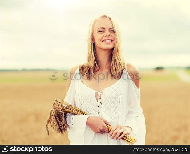 country, nature, summer holidays, vacation and people concept - smiling young woman in white dress with spikelets walking along on cereal field. happy young woman with spikelets on cereal field