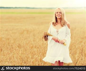 country, nature, summer holidays, vacation and people concept - smiling young woman in white dress with spikelets walking along on cereal field. happy young woman with spikelets on cereal field