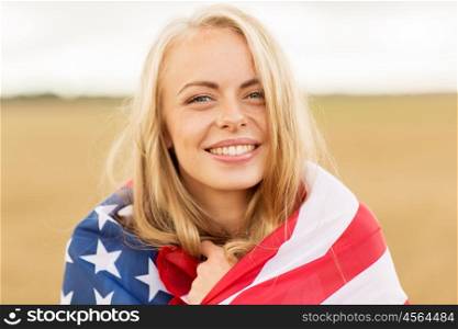 country, patriotism, independence day and people concept - happy smiling young woman wrapped into national american flag on cereal field