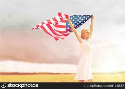 country, patriotism, independence day and people concept - happy smiling young woman in white dress with national american flag on cereal field. happy woman with american flag on cereal field