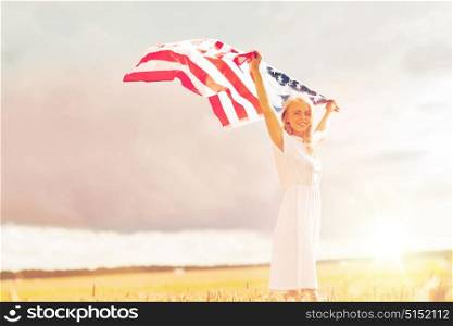 country, patriotism, independence day and people concept - happy smiling young woman in white dress with national american flag on cereal field. happy woman with american flag on cereal field