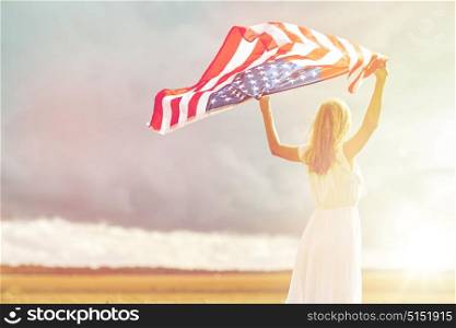 country, patriotism, independence day and people concept - happy young woman in white dress with national american flag on cereal field. happy woman with american flag on cereal field