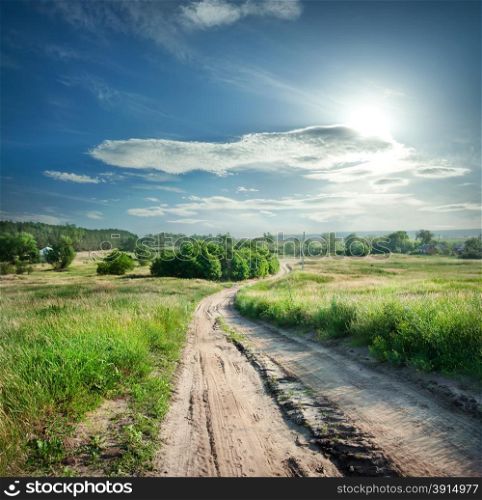 Country road in field with green grass under a dramatic sky