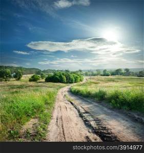 Country road in field with green grass under a dramatic sky
